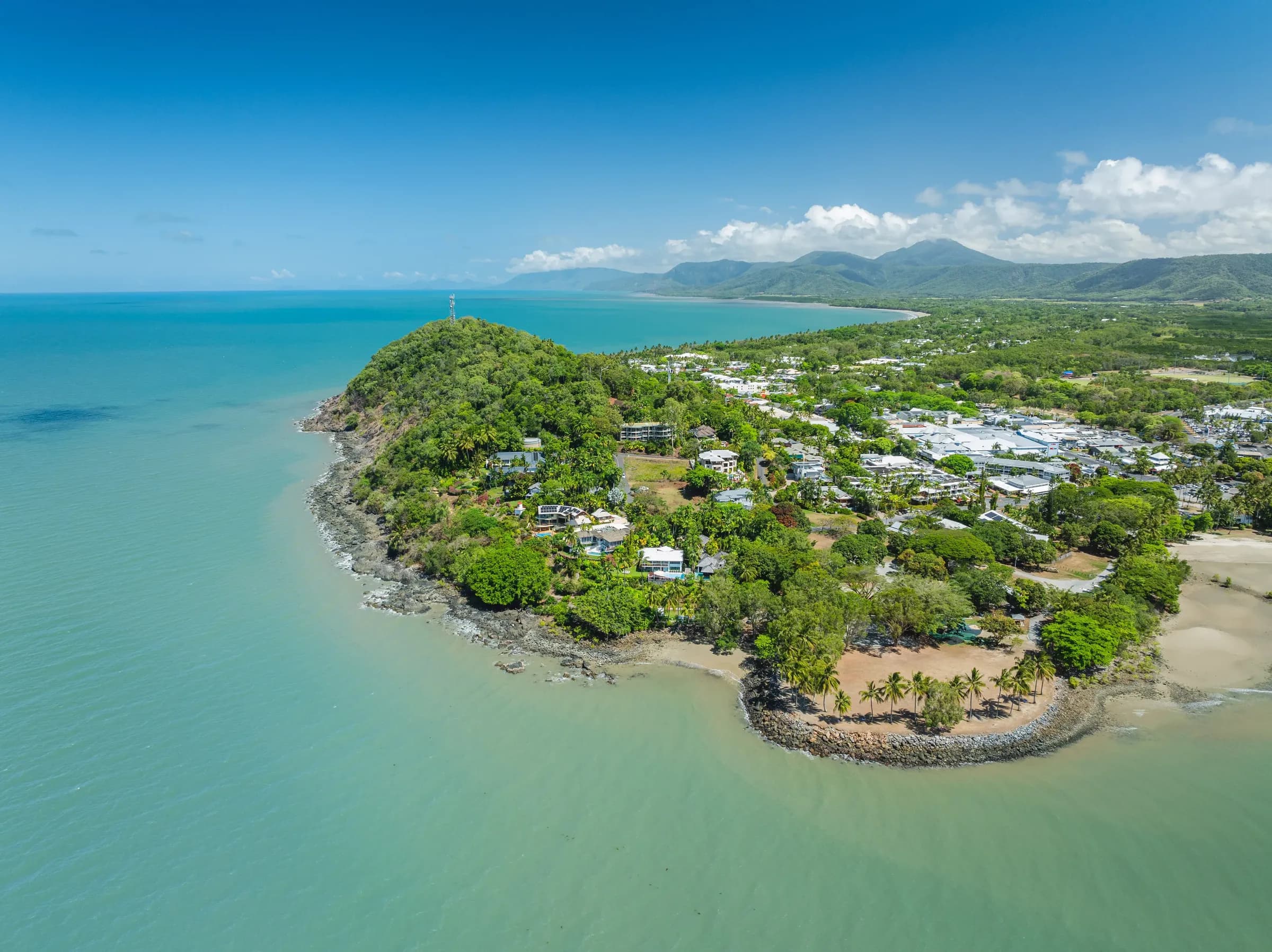 Aerial drone view of Port Douglas headland and Flagstaff Hill surrounded by turquoise Coral Sea waters, with mountains in the background