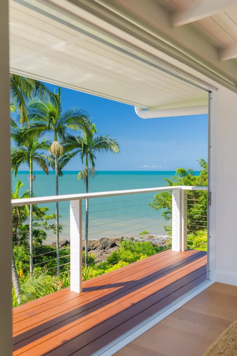 Private timber balcony opening to turquoise ocean views framed by coconut palms and tropical greenery at Havana, Port Douglas