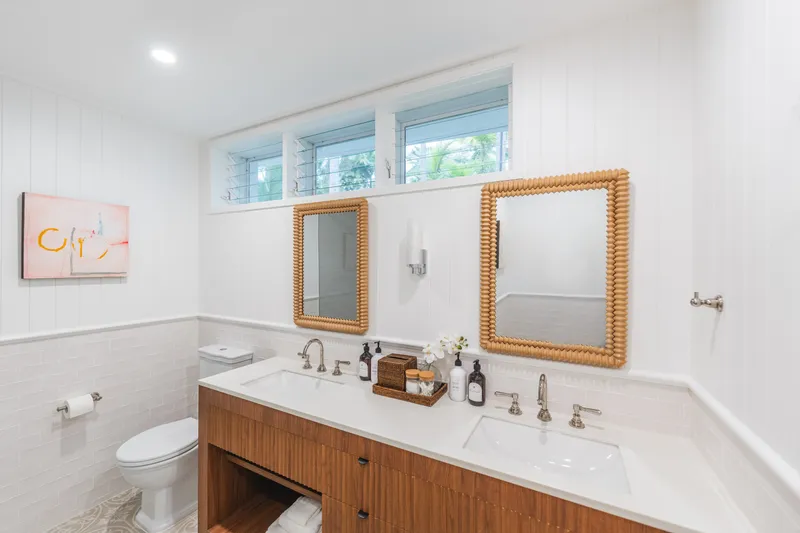 Bright bathroom at Havana Port Douglas featuring a timber double vanity with rattan-framed mirrors and white panelled walls