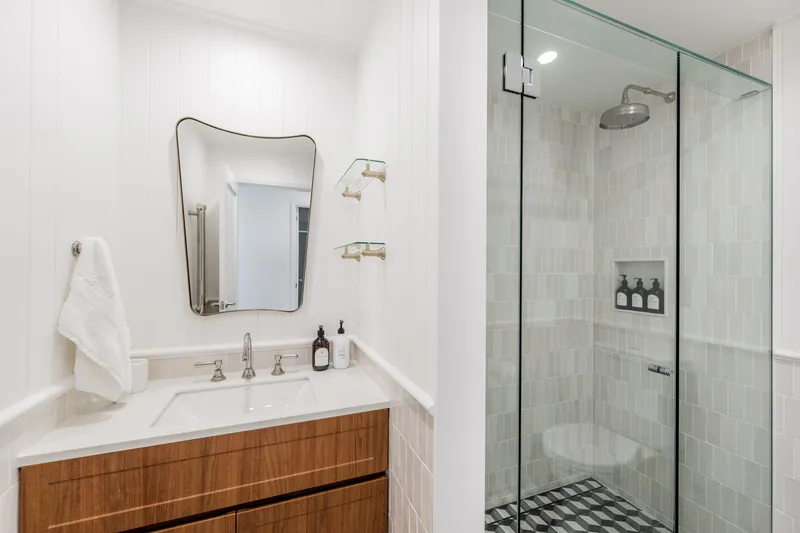 Modern bathroom with timber vanity, shaped mirror, and glass-enclosed shower with handmade tiles at Havana, Port Douglas