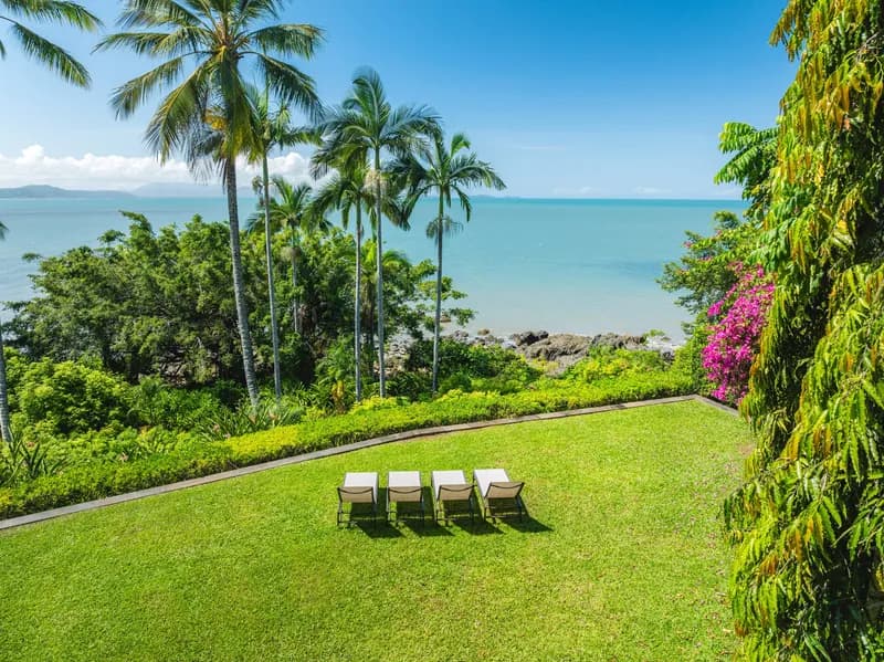 Manicured beachfront lawn with four sun lounges beneath palm trees, bougainvillea, and panoramic Coral Sea views at Havana, Port Douglas