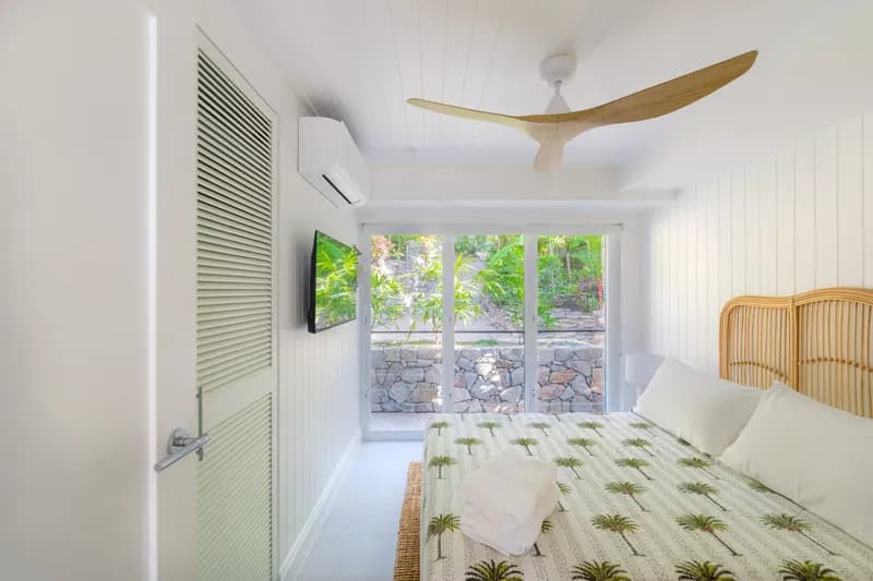 Alternate view of a Havana Port Douglas bedroom showing wall-mounted TV, louvred wardrobe doors, timber ceiling fan, and sliding glass door with tropical garden views