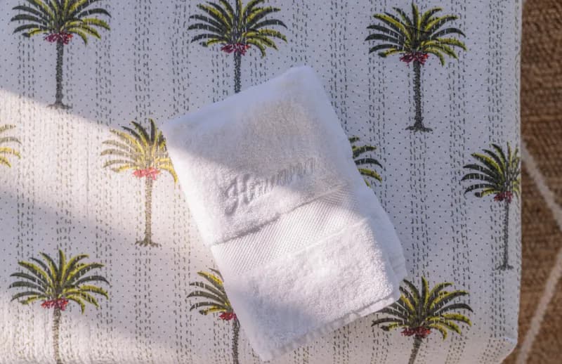 Close-up of an embroidered Havana-branded white towel resting on a palm-tree-print bedspread at Havana Port Douglas