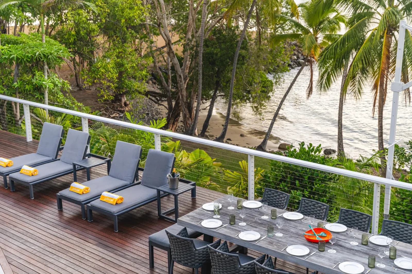 Elevated timber deck at Havana Port Douglas with sun loungers and a set dining table overlooking the beach and palm trees