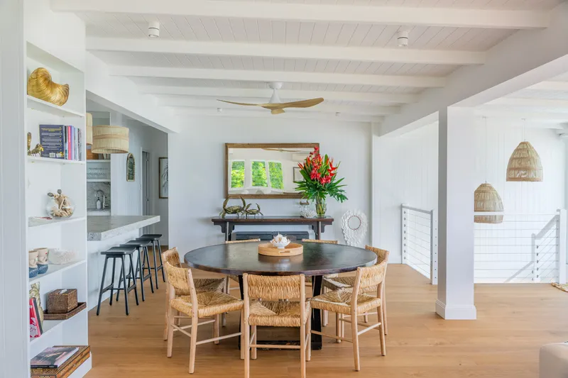 Dining area at Havana Port Douglas with large round dark timber table, woven rattan chairs, built-in bookshelves, tropical flower arrangement, and rattan pendant lights