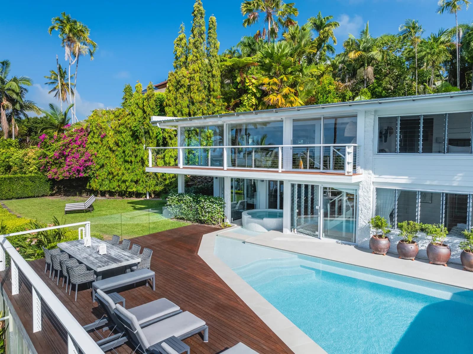 Elevated exterior view of Havana Port Douglas showing the two-level white weatherboard house, pool, timber deck with outdoor dining, bougainvillea, and tropical canopy