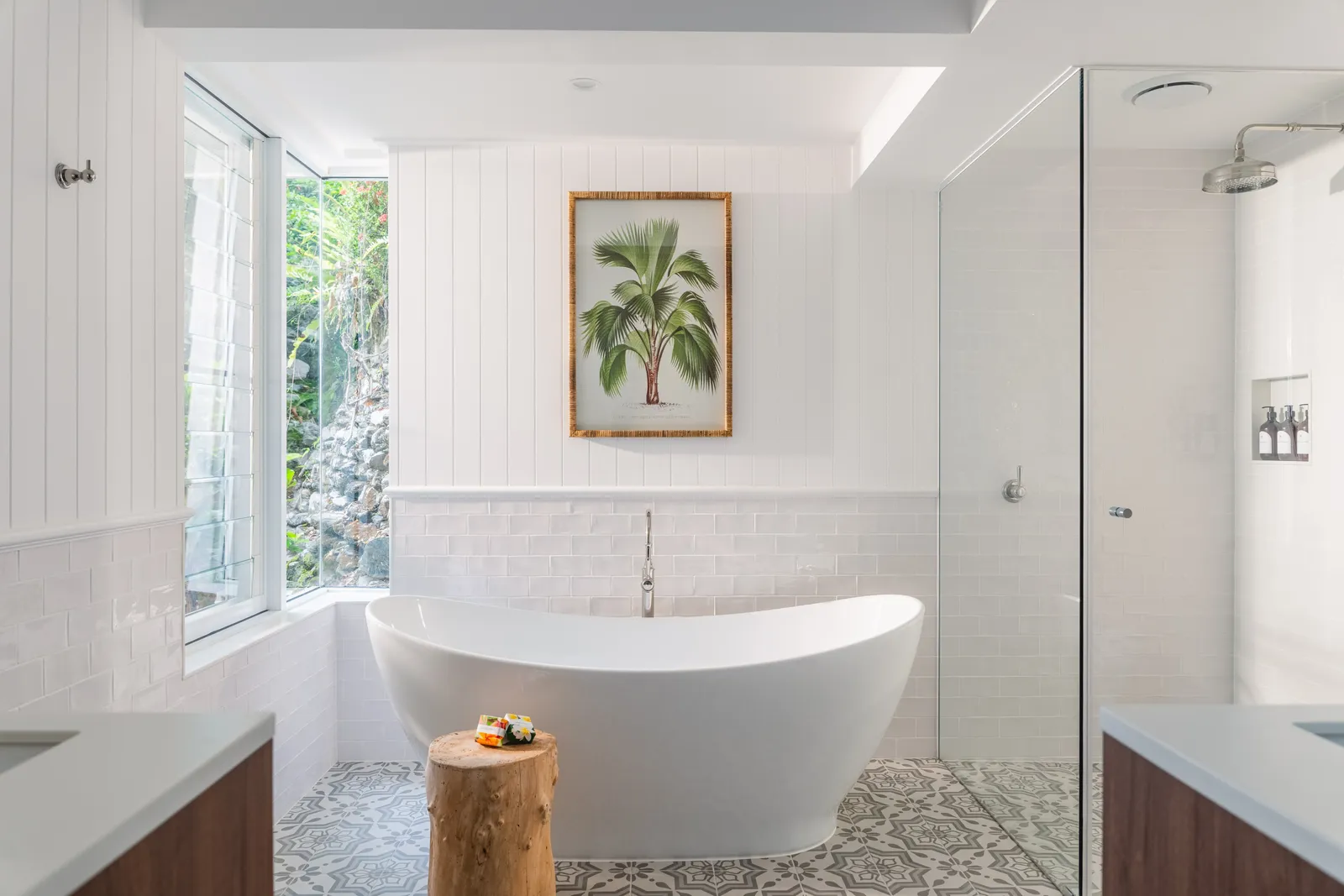 Luxurious bathroom at Havana Port Douglas with freestanding bathtub, palm tree artwork, patterned floor tiles, and garden-view window