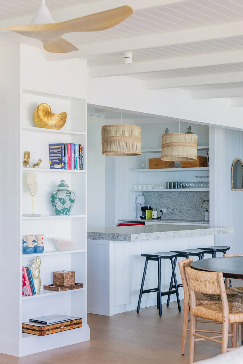 Kitchen and breakfast bar at Havana Port Douglas with stone benchtops, rattan pendant lights, black bar stools, curated bookshelf, and timber ceiling fan