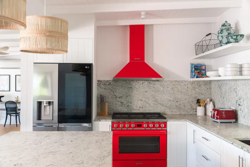 Kitchen detail at Havana Port Douglas featuring a bold red Smeg gas range and matching rangehood, marble-look splashback, LG fridge, and rattan pendant light