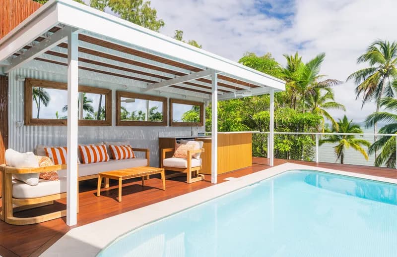 Covered pool cabana with outdoor lounge seating, orange-striped cushions, and timber deck beside the pool surrounded by palm trees at Havana, Port Douglas