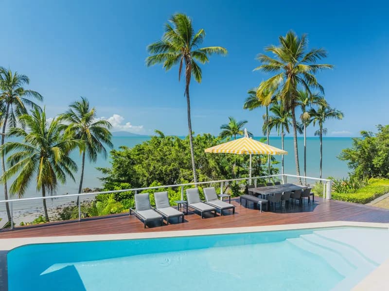 Pool deck with sun lounges and outdoor dining under a yellow-striped umbrella, overlooking palm trees and the Coral Sea at Havana, Port Douglas