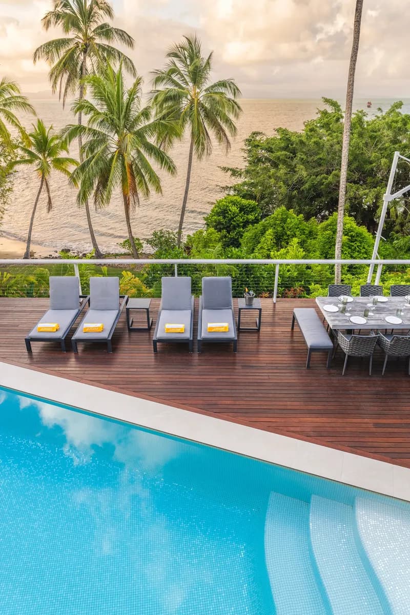 Pool and timber deck at Havana Port Douglas with sun loungers and outdoor dining framed by palm trees and ocean views at dusk
