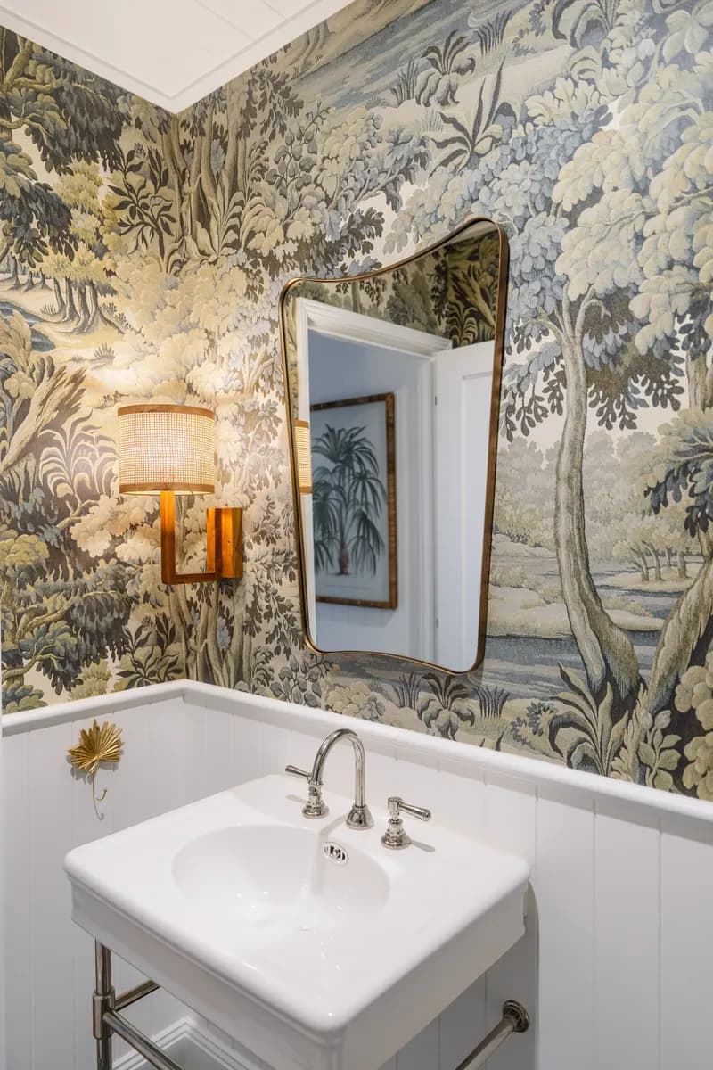 Elegant powder room at Havana Port Douglas with tropical forest wallpaper, brass-framed mirror, wall sconce, and pedestal basin