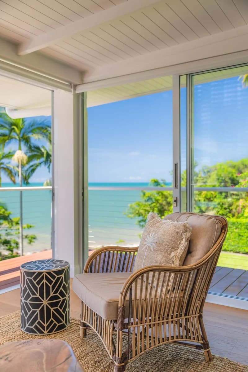 Rattan armchair with cushions and decorative side table beside sliding glass doors opening to Coral Sea views at Havana, Port Douglas
