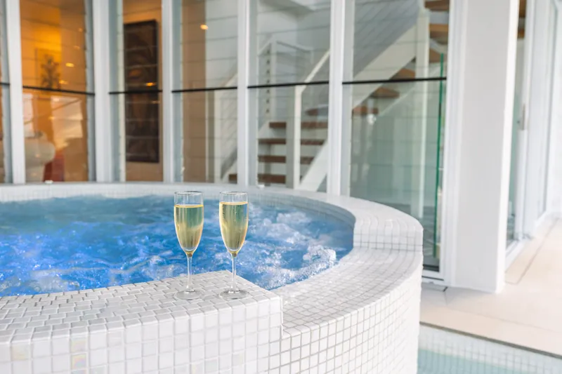 Two glasses of champagne on the edge of the mosaic-tiled spa at Havana Port Douglas with the interior staircase visible behind