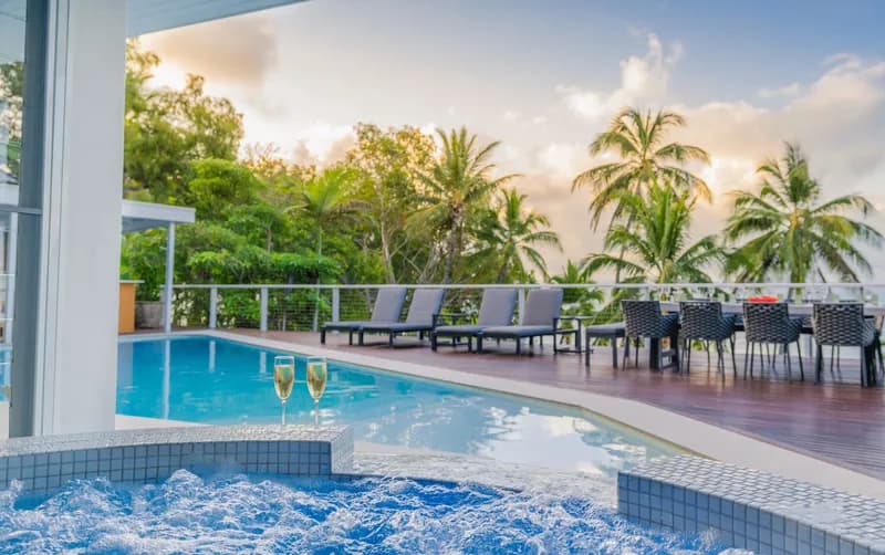 View from the bubbling spa across the pool deck at Havana Port Douglas with champagne glasses, loungers, and palm trees at sunset