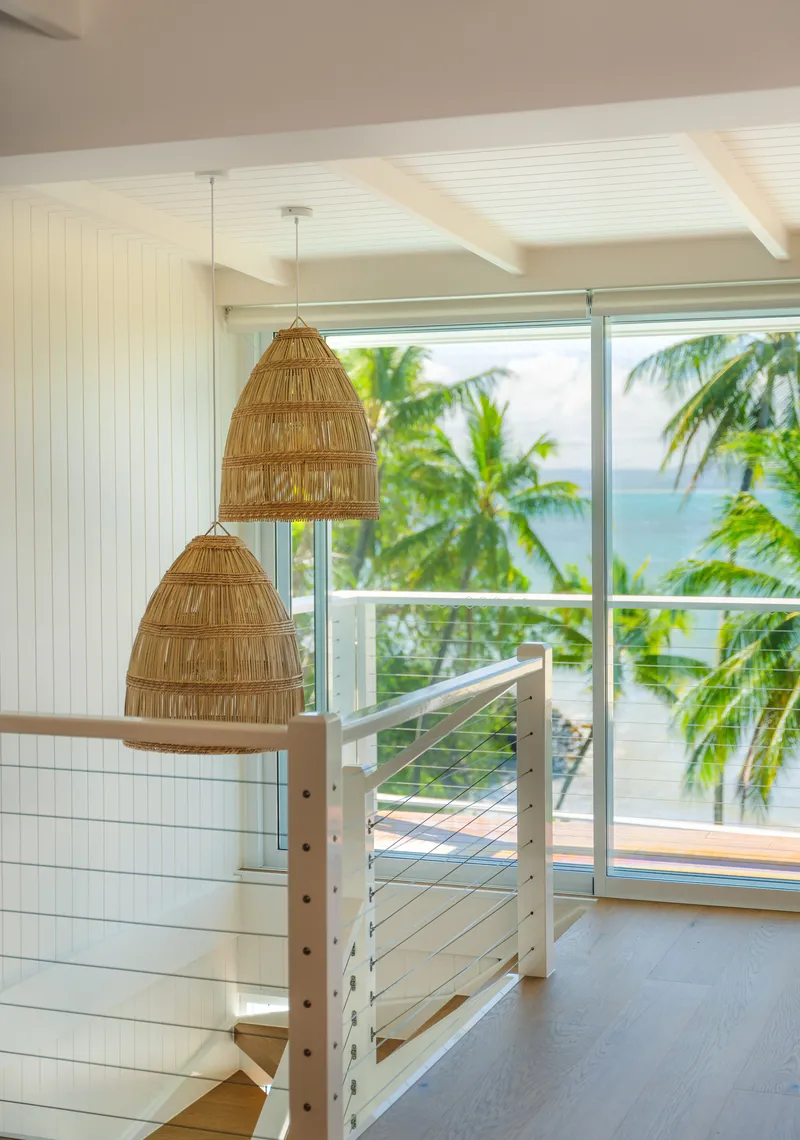 Open stairwell with woven rattan pendant lights, timber handrail, and floor-to-ceiling windows framing palm trees and ocean at Havana, Port Douglas