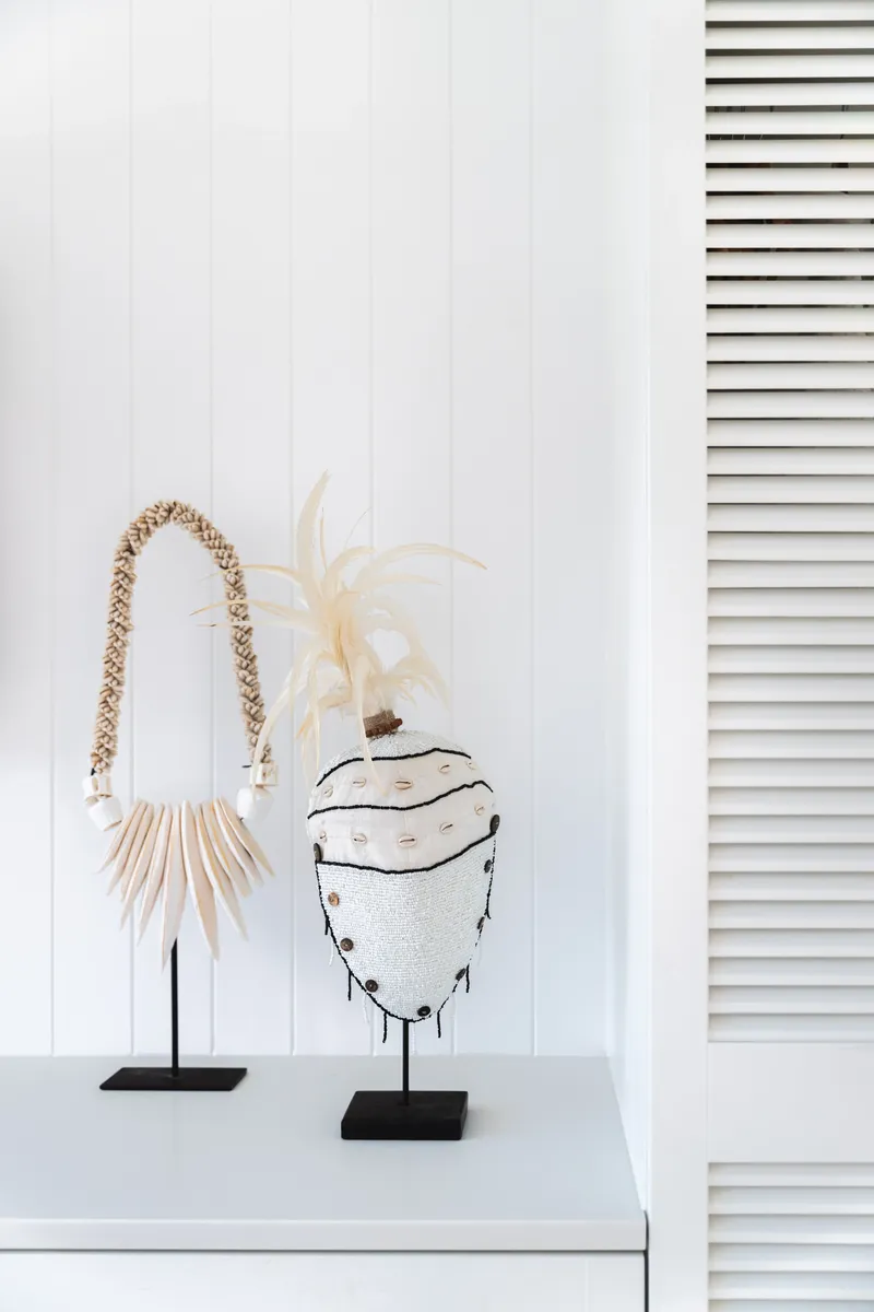 Handcrafted tribal shell necklace and beaded headdress sculptures displayed on black stands against white VJ panelling and louvred doors at Havana Port Douglas